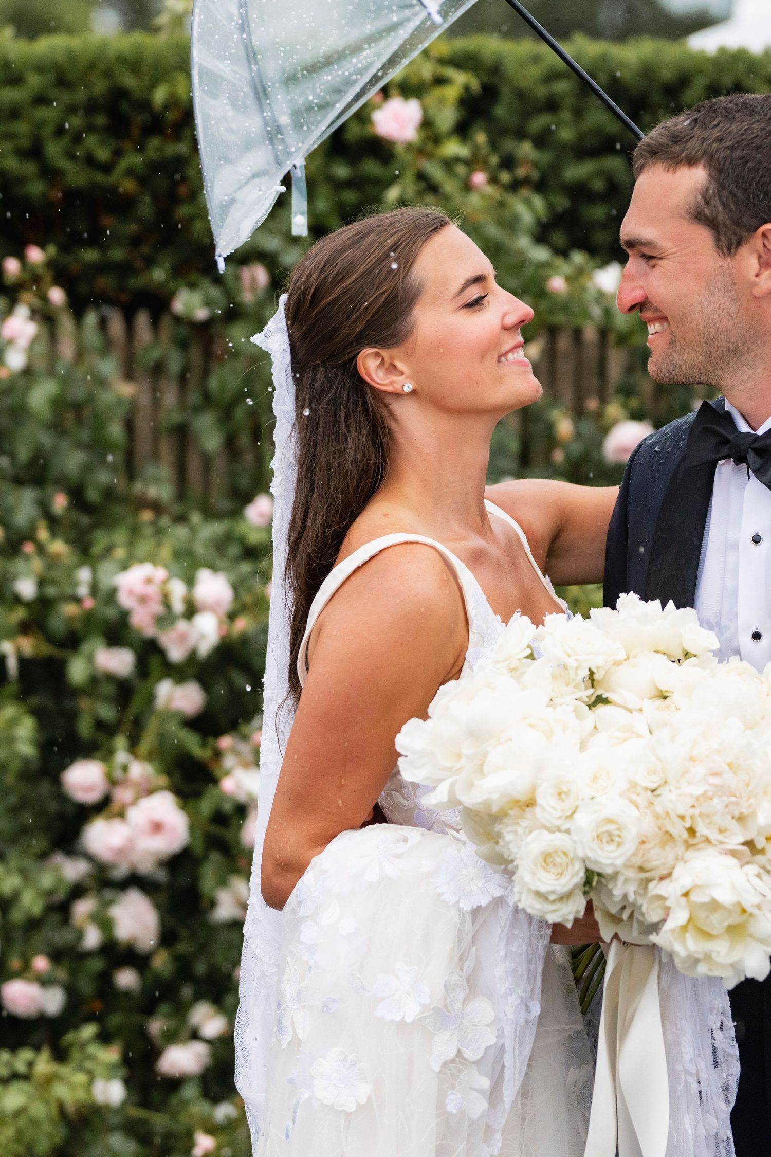 Couple sharing intimate moments under an umbrella surrounded by blooming white roses.