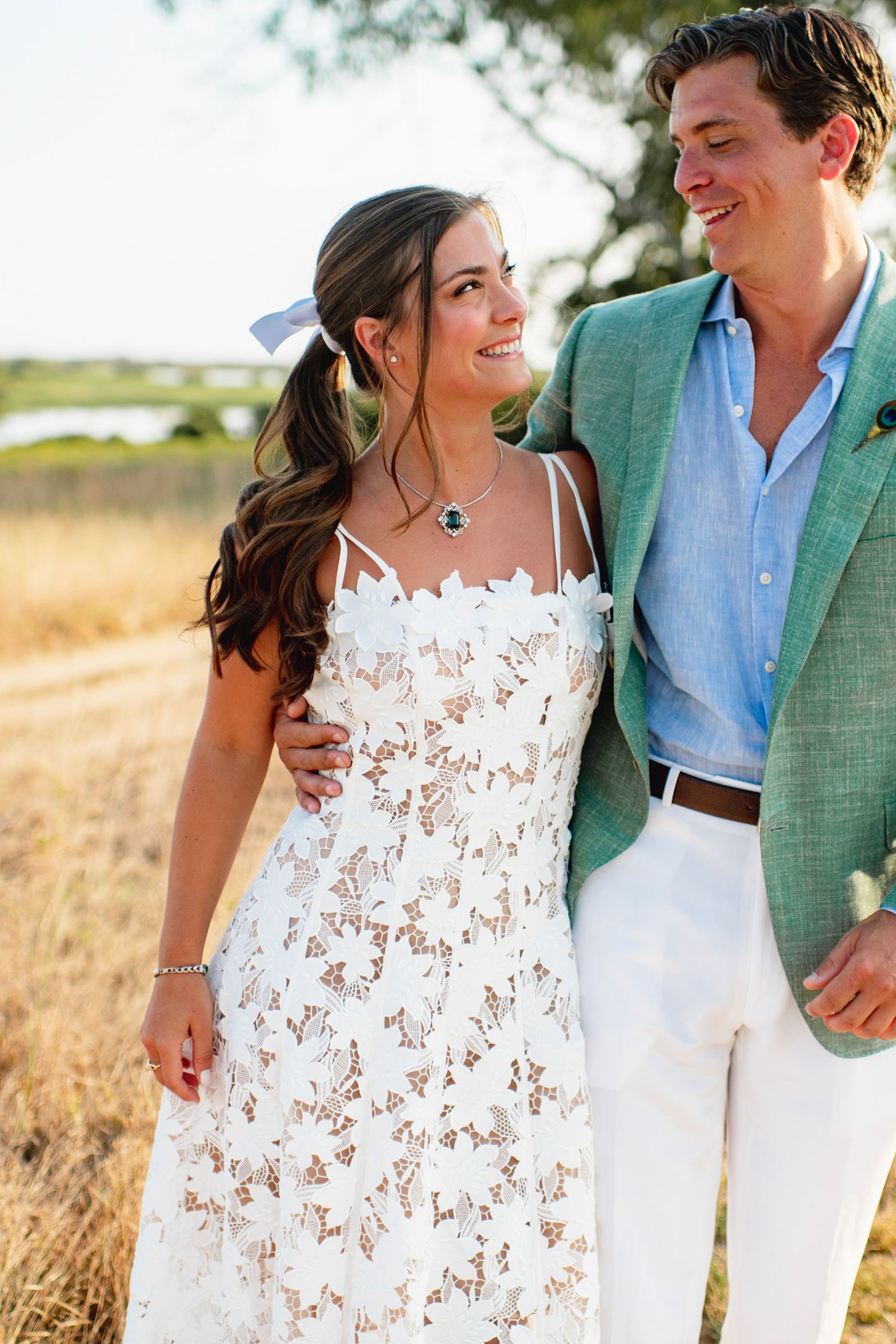 Couple in white dress and green blazer share intimate moments in a golden field during sunset photo session.