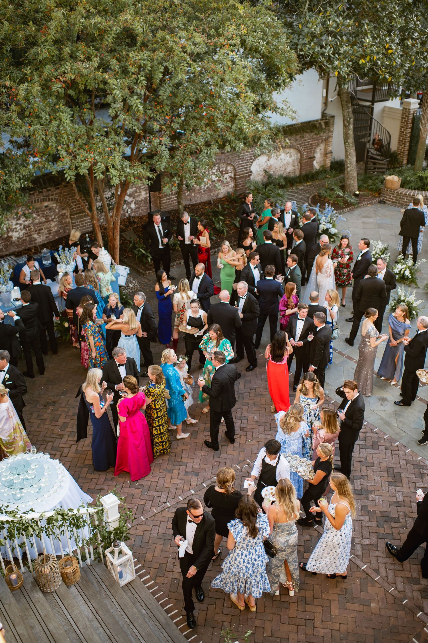 Aerial view of wedding guests mingling and socializing during an outdoor garden reception on a brick patio.