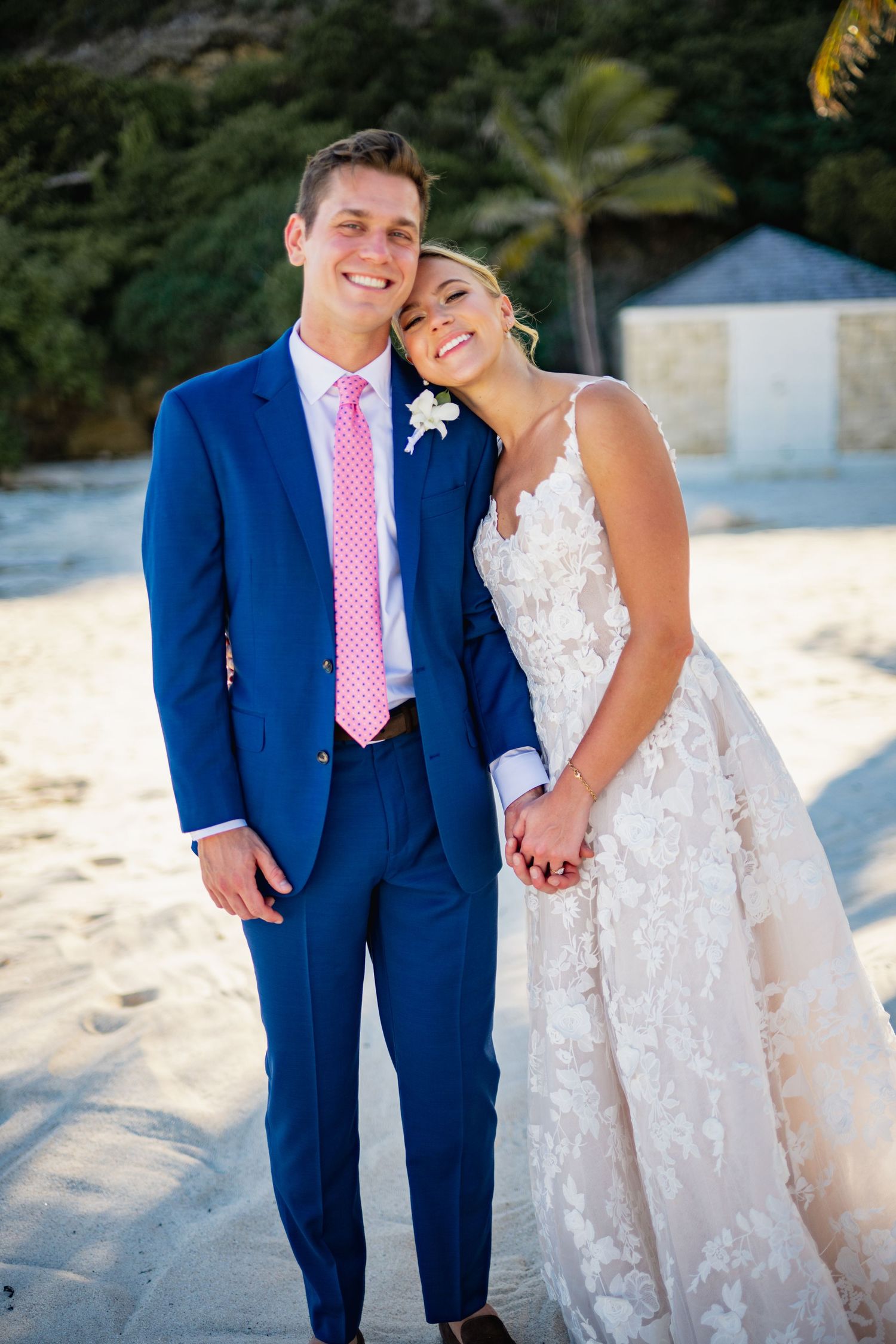 Couple in formal wedding attire share intimate moments on a sunny beach with white sand and ocean views.