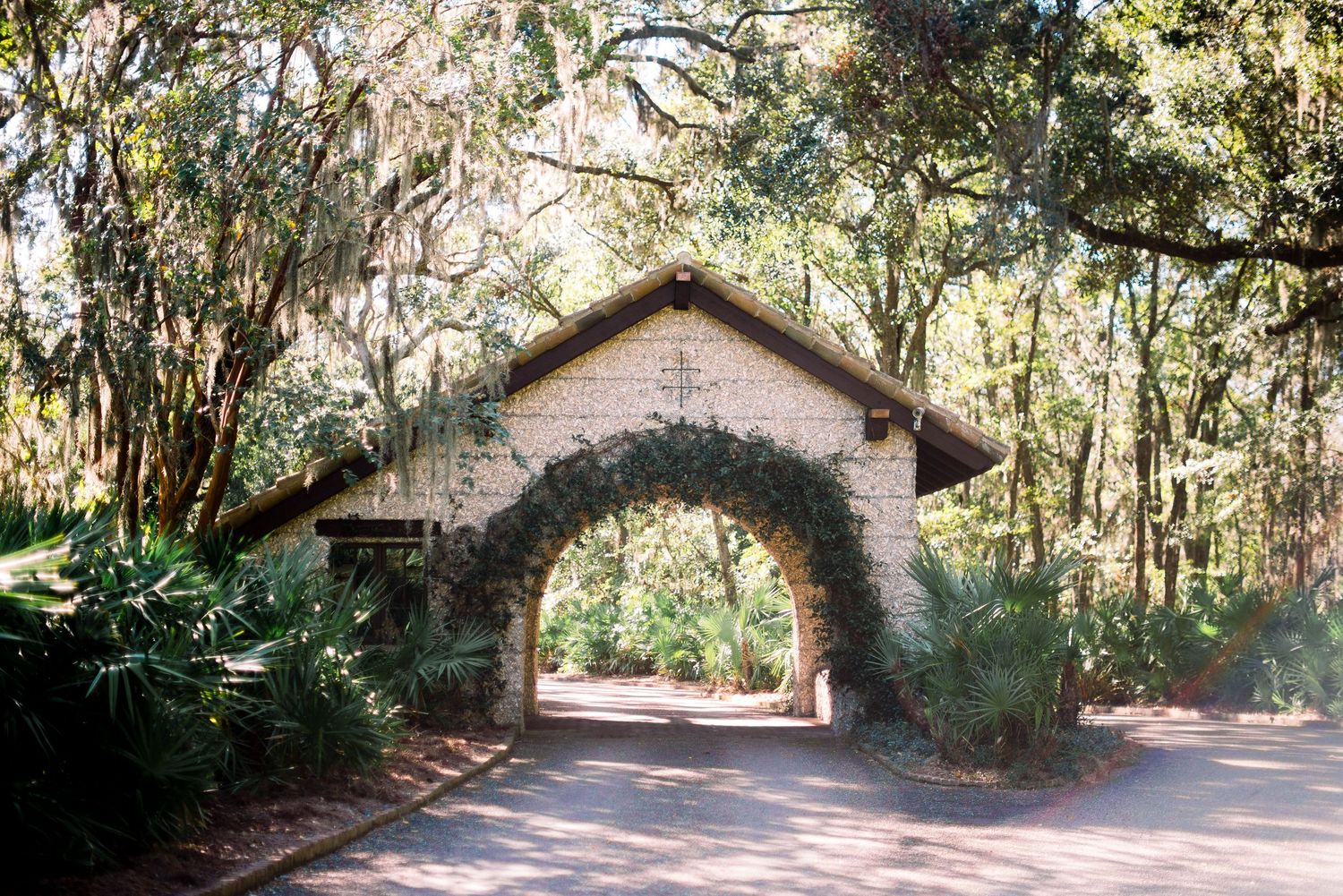 A series of connected brick archways form a shaded tunnel pathway through a lush green forest canopy.