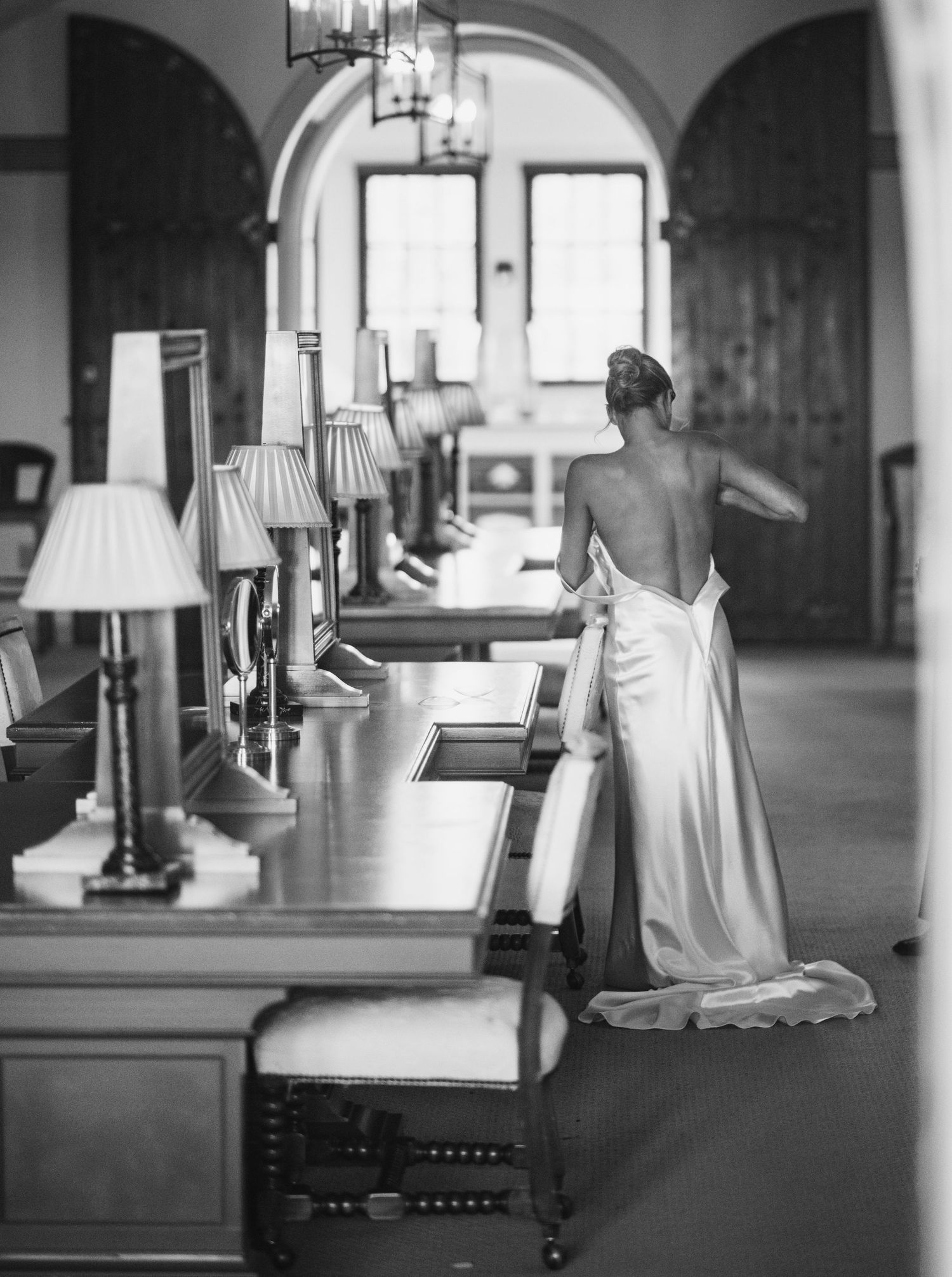 A black and white photograph of multiple table lamps with white shades arranged in a row along a hallway.
