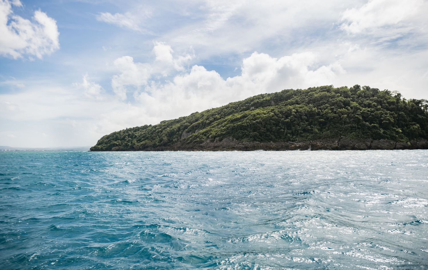 Scenic panoramic view of a tropical island coastline with turquoise waters and lush green hills under blue skies.