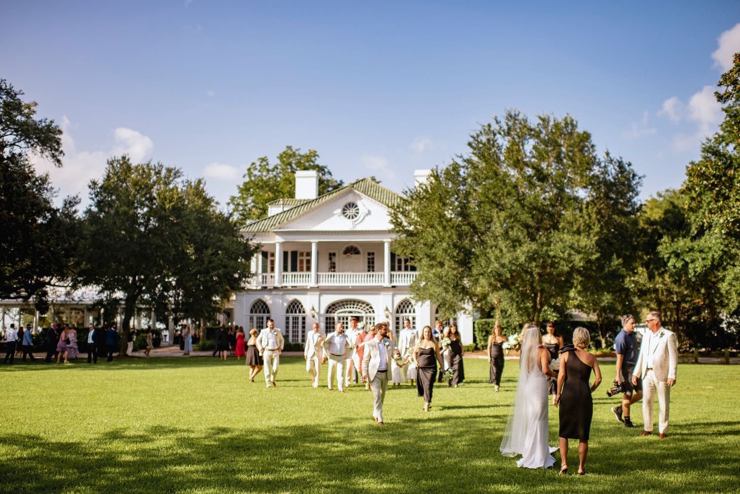 Wedding guests gather on a lush green lawn outside the elegant Lowndes Grove with columns and arched windows.