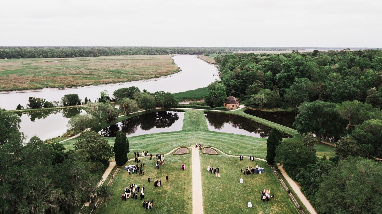 Panoramic aerial view of a winding river through green countryside with walking paths and scattered trees.