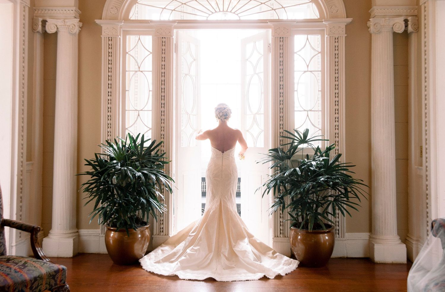 A panoramic view of an elegant white wedding dress displayed in a grand room with ornate columns and potted palms.