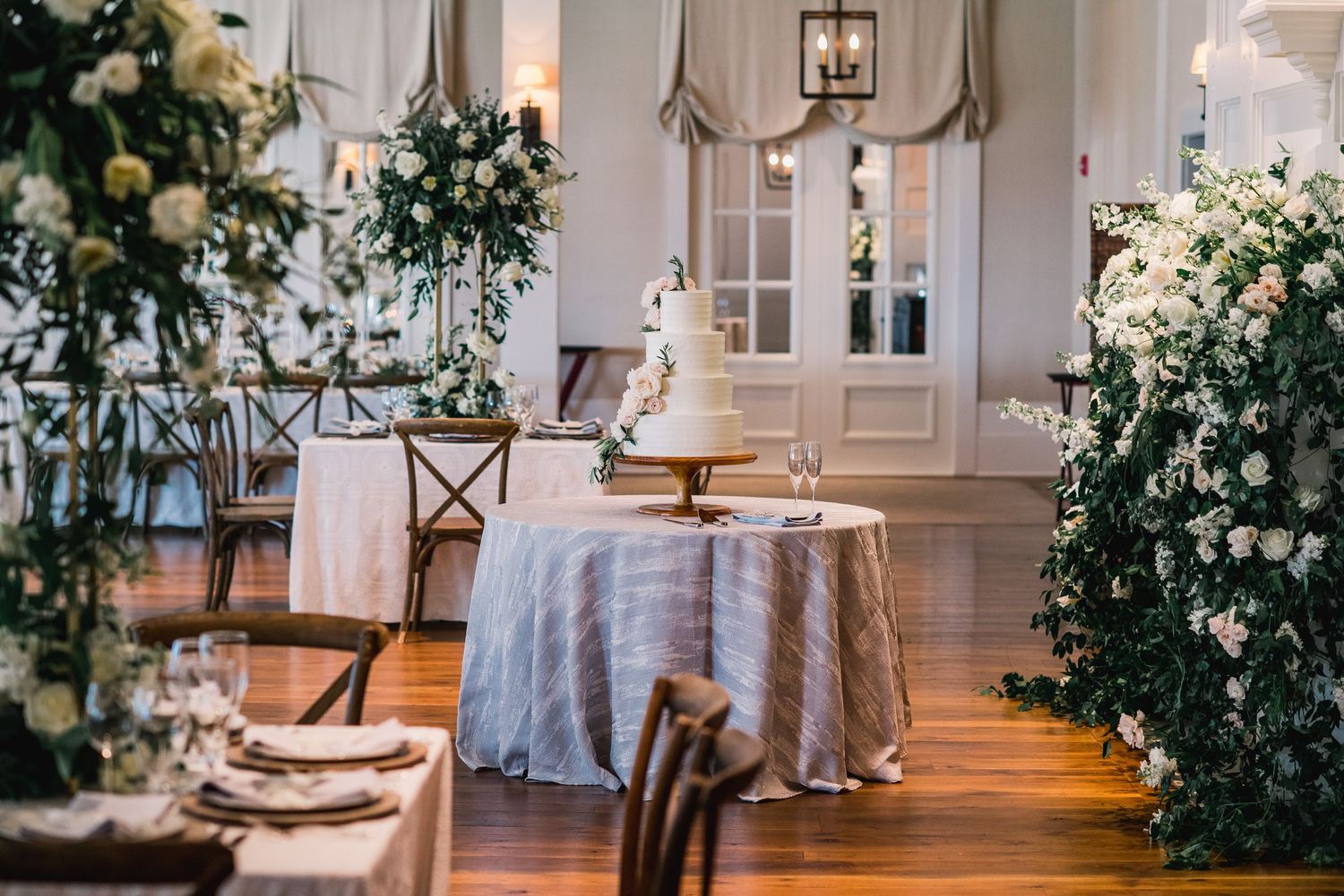 Elegant white wedding venue interior decorated with lush greenery and floral arrangements along the aisle.