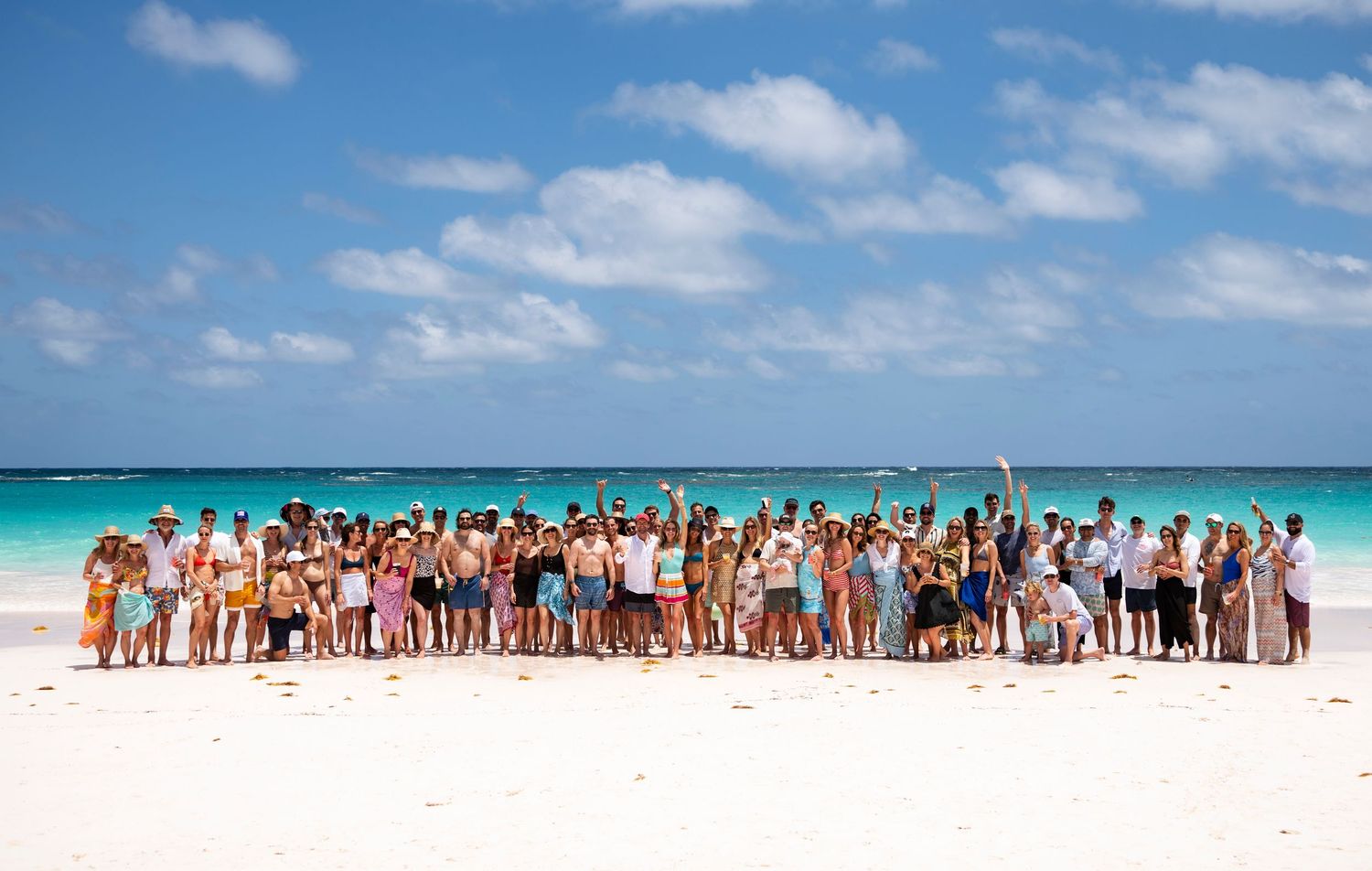 Large group of wedding guests lined up along a pristine white sand beach with turquoise waters in the background.