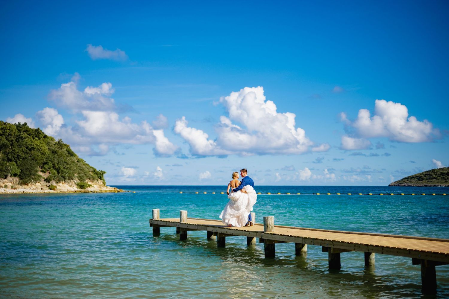 Couple standing on wooden pier overlooking crystal blue Caribbean waters.