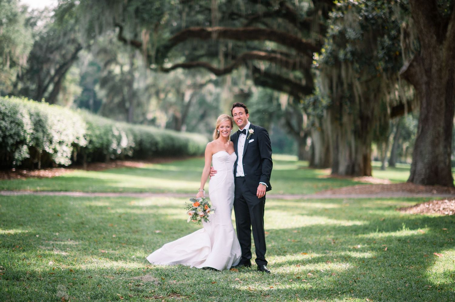 Couple poses for romantic wedding photos beneath Spanish moss draped oak trees in a Southern garden setting.