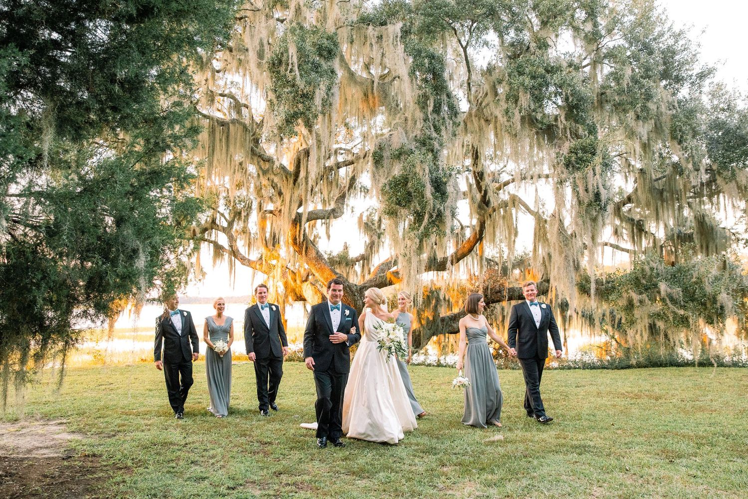 Wedding party poses under Spanish moss-draped trees during golden hour at a romantic outdoor ceremony.