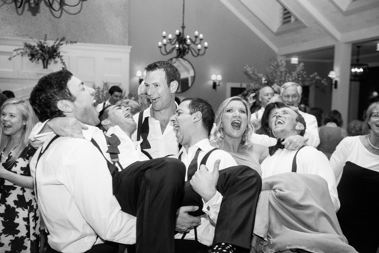 Black and white photo of wedding guests dancing and celebrating on a dance floor at a reception party.