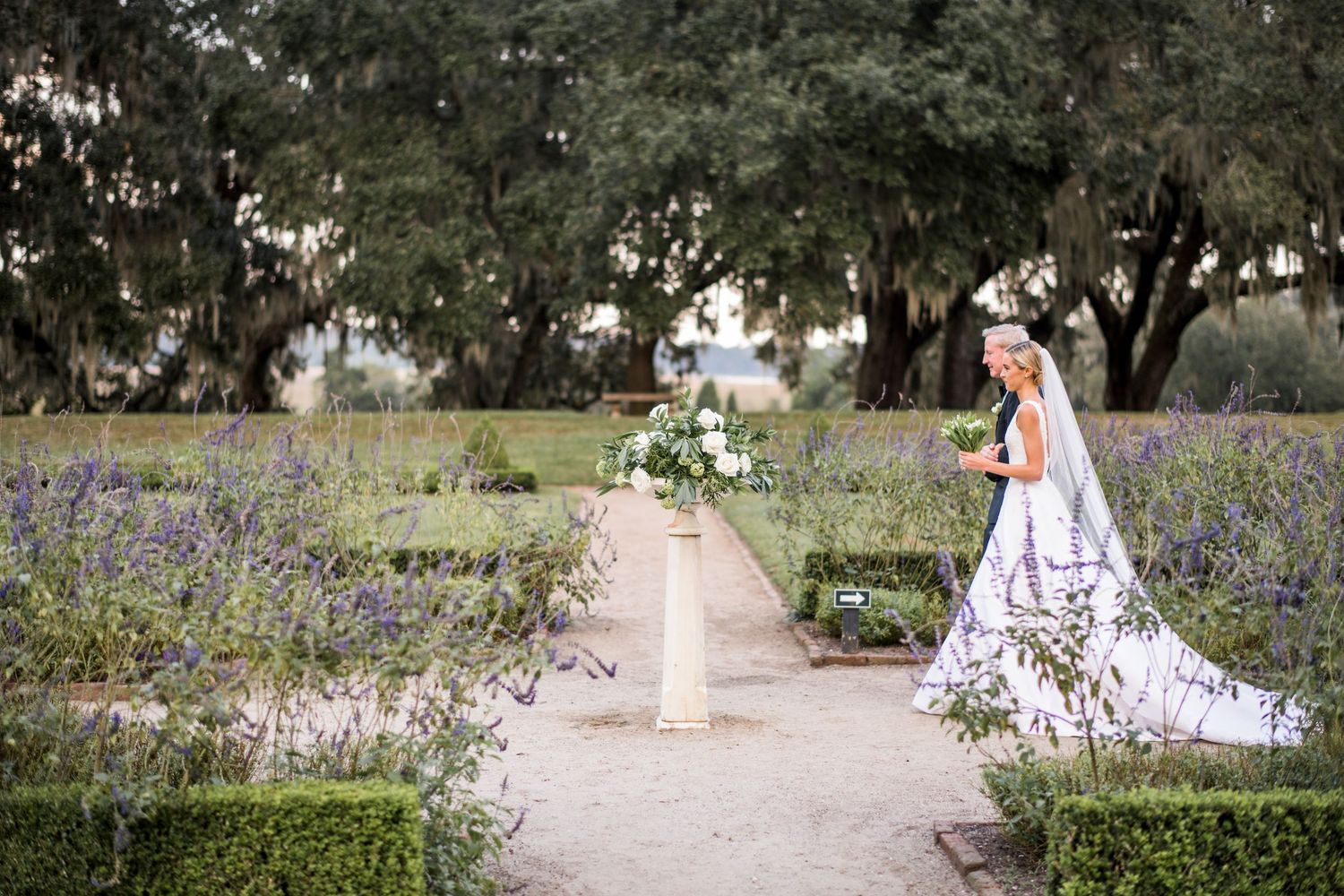 A person walks through a garden path lined with blooming bluebonnets and white wildflowers in a serene park setting.