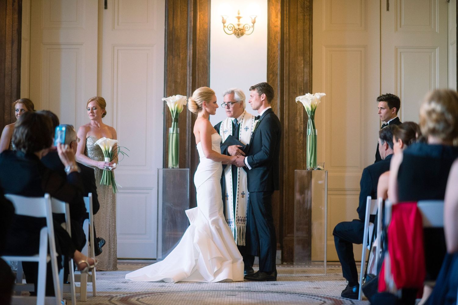 Wedding party enters grand ballroom through white double doors as guests applaud during reception entrance.