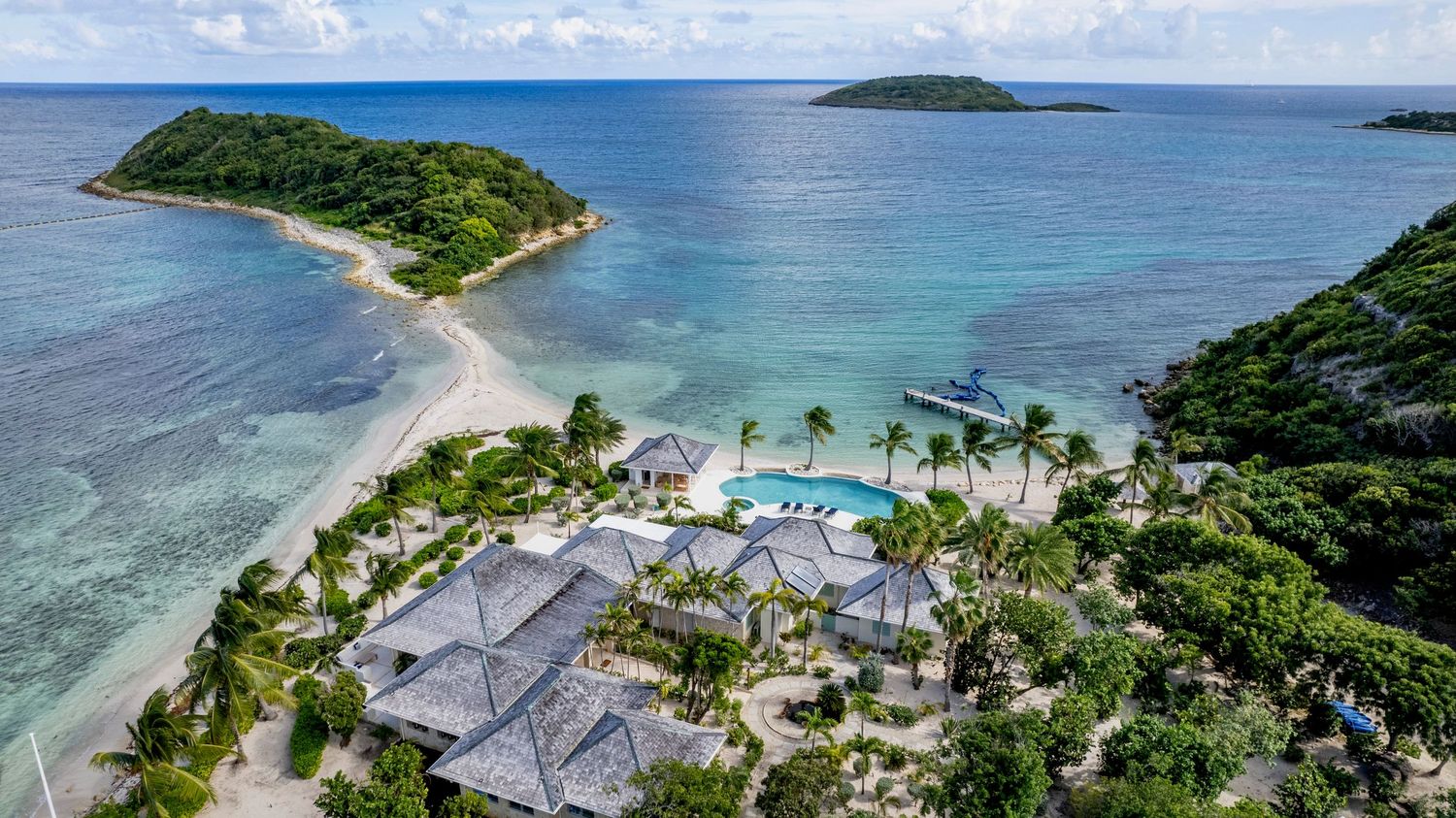 Aerial view of a luxury island resort in Antigua with swimming pools and tropical landscaping surrounded by crystal clear waters.