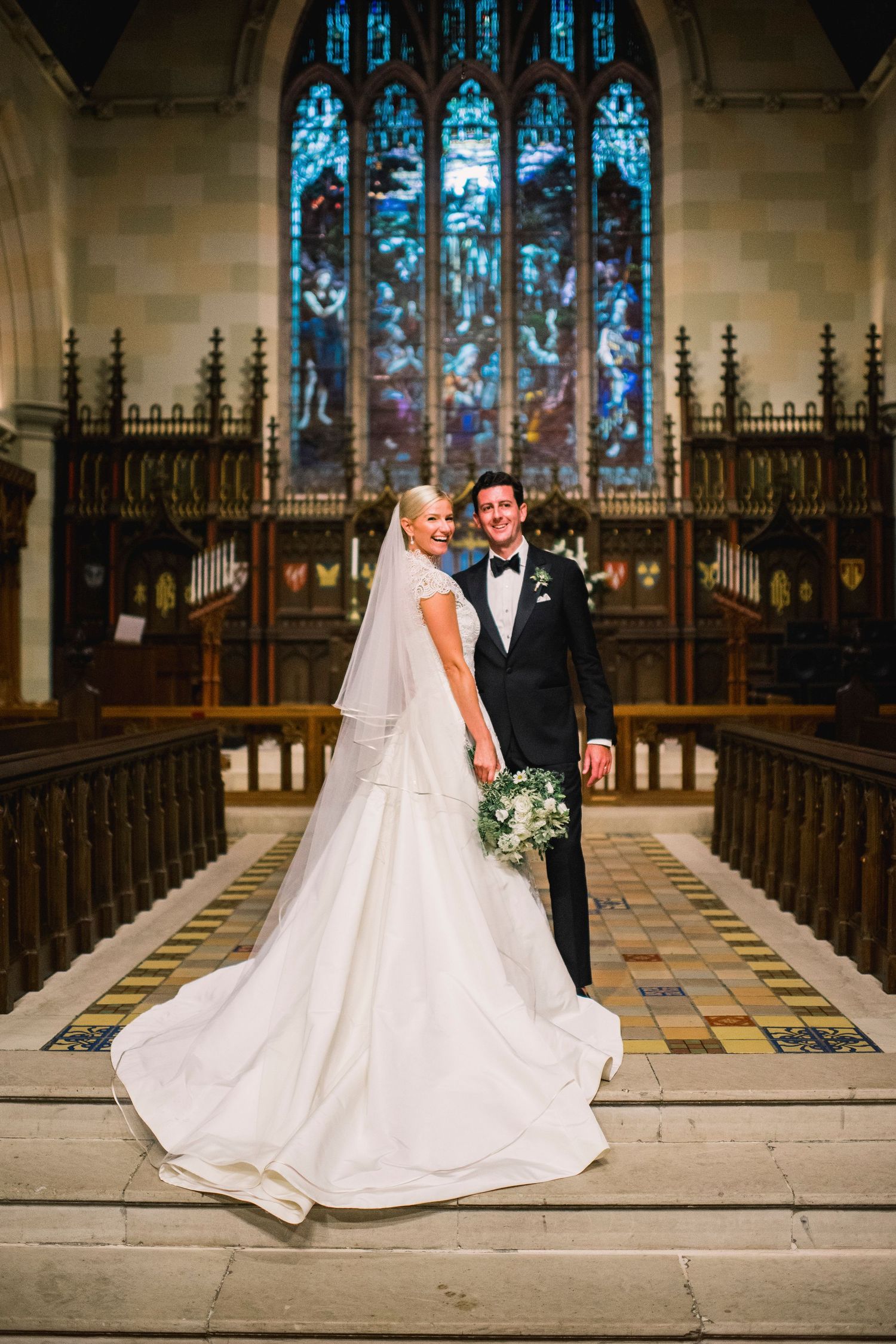 Wedding couple posing in front of stunning stained glass windows inside a grand church.