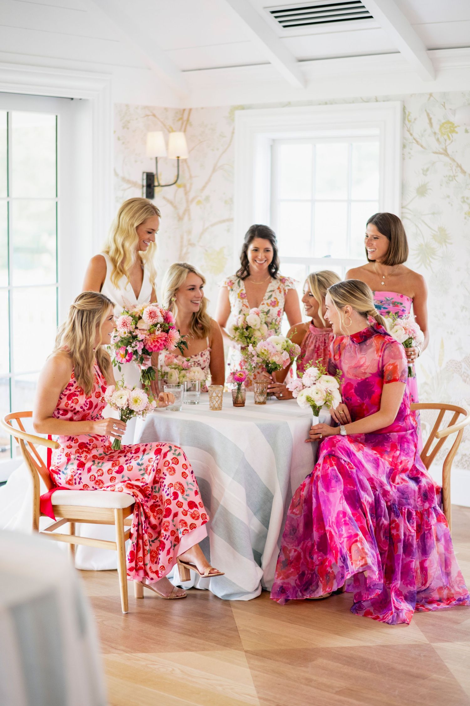 Bridesmaids in vibrant pink and floral dresses gather at elegant tables during a wedding reception.