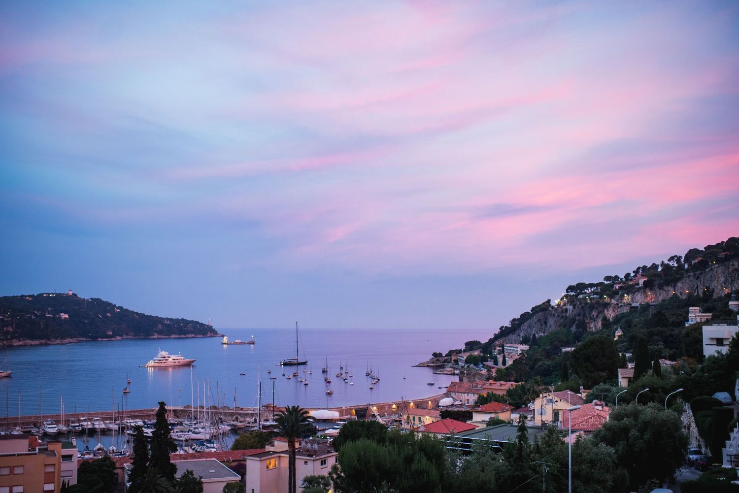 Coastal village at sunset in Beau Lieu Sur Mer France with boats in the harbor and pink-tinged clouds over the Mediterranean.