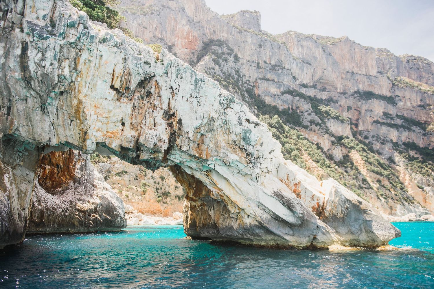 Natural stone arch formation over bright turquoise waters along a dramatic coastal cliff face.