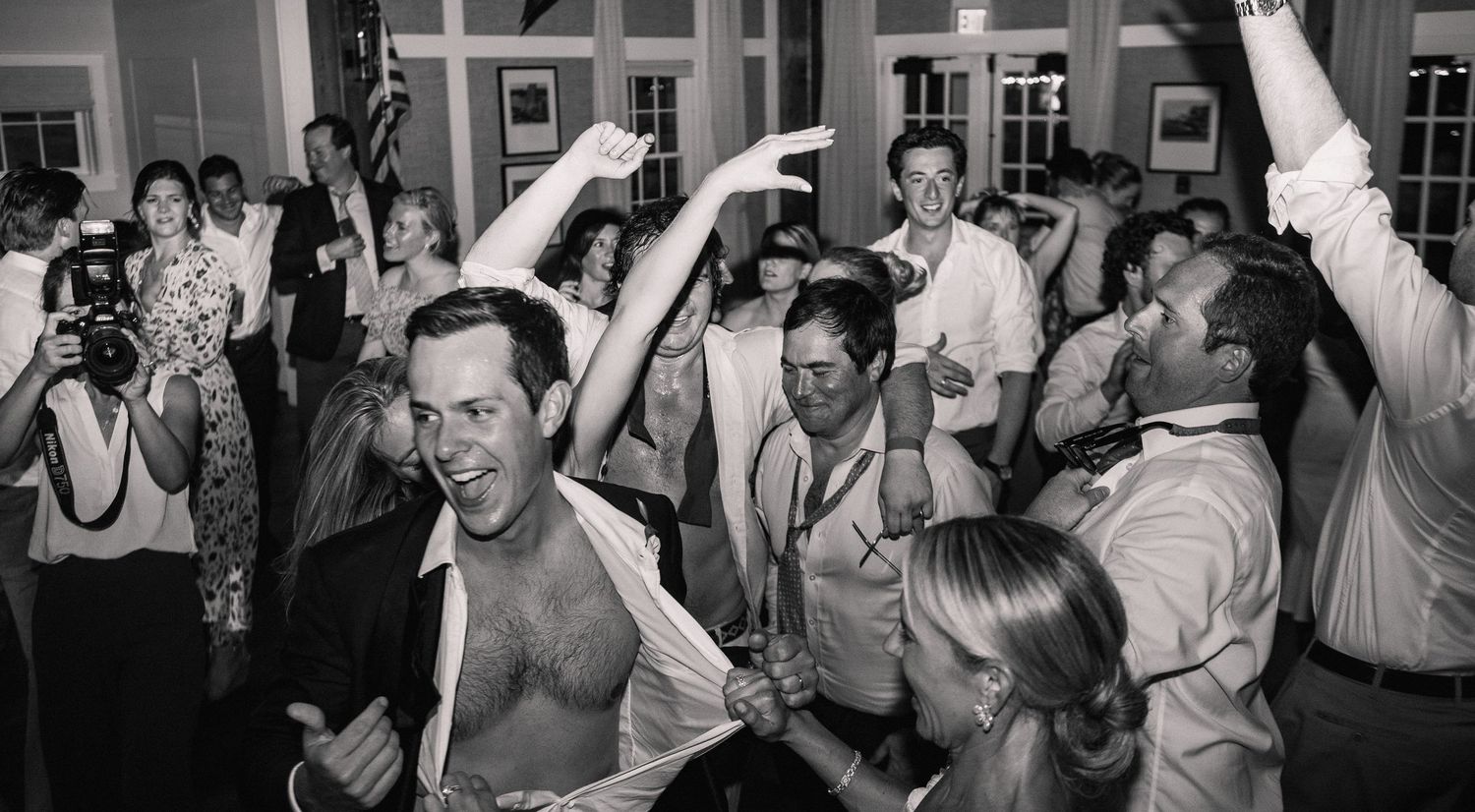 Panoramic view of wedding guests dancing and celebrating at an indoor reception.