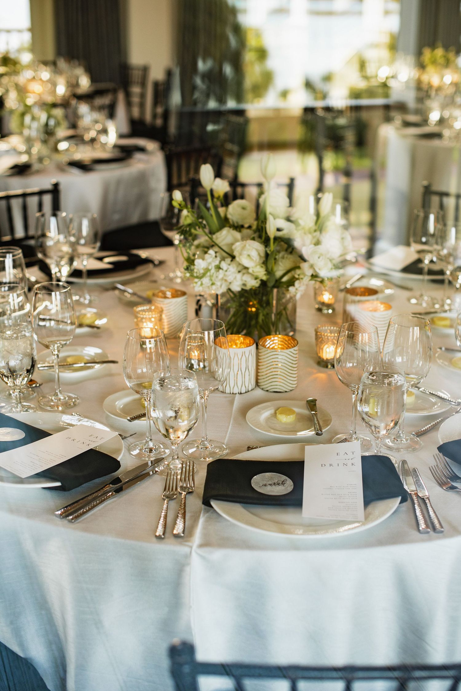 Elegant wedding reception table settings with white linens, crystal glassware, and soft floral centerpieces.