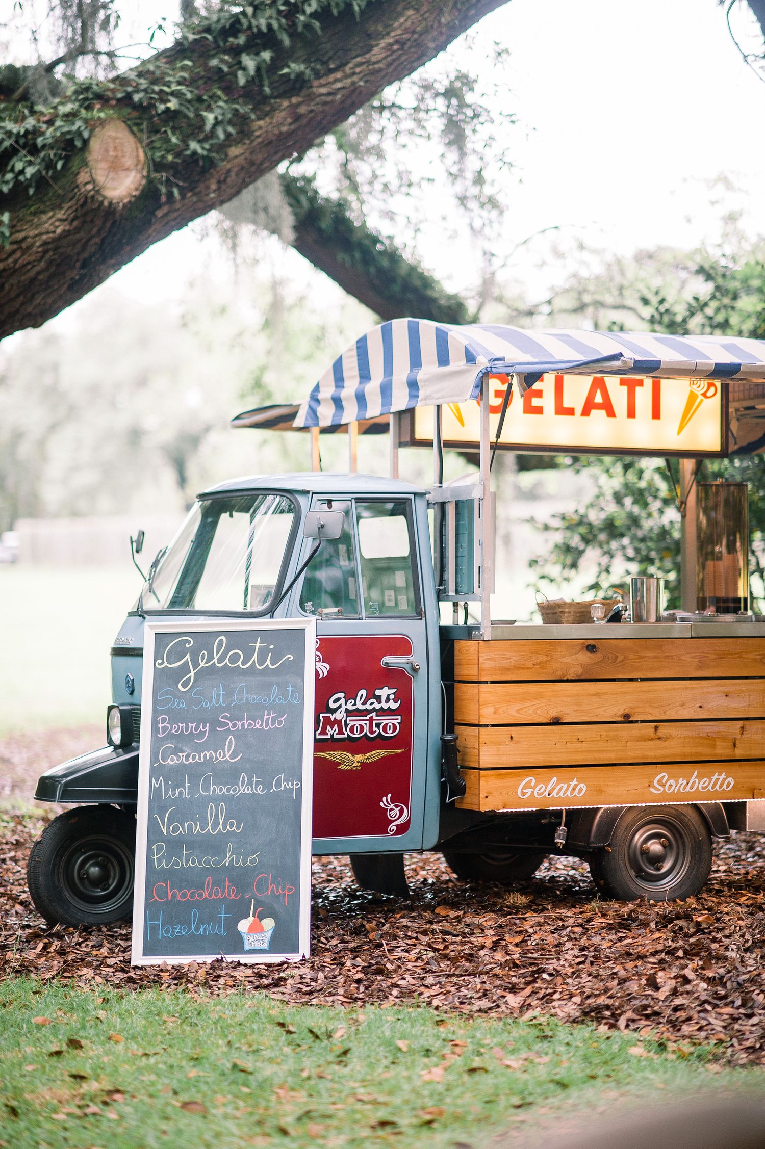 Vintage food truck setup with chalkboard menus and gelato signs under shady trees at an outdoor event.