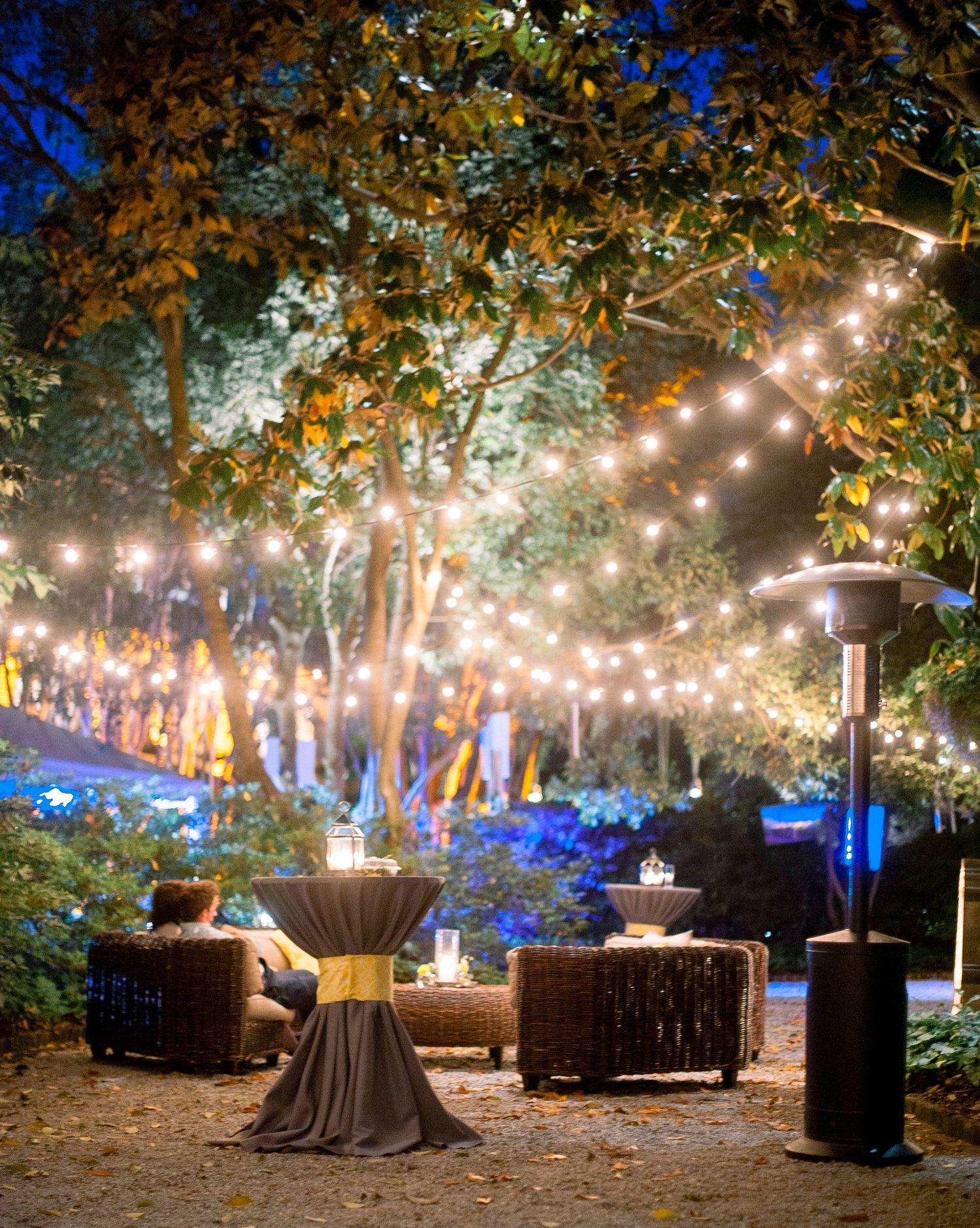 Enchanting outdoor event space with string lights illuminating tables and trees creating a magical forest atmosphere.