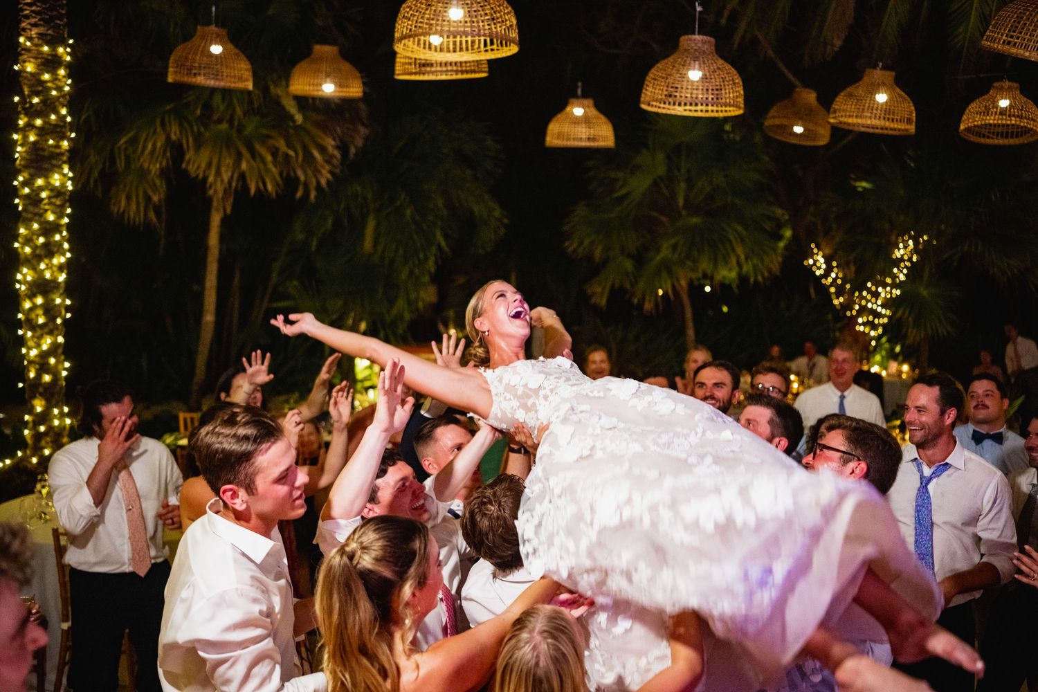 Wedding reception dance floor filled with guests celebrating under hanging wicker lanterns and string lights.