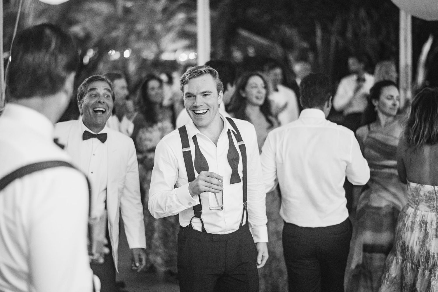 A happy couple shares a joyful moment together on their wedding day, surrounded by smiling guests at the reception.