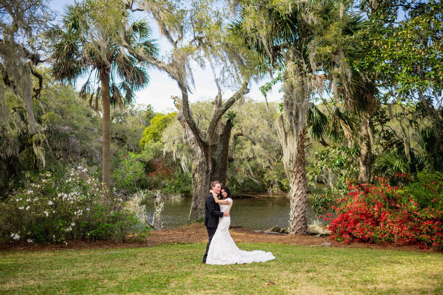 A romantic outdoor wedding ceremony takes place under Spanish moss draped oak trees in a lush garden setting.