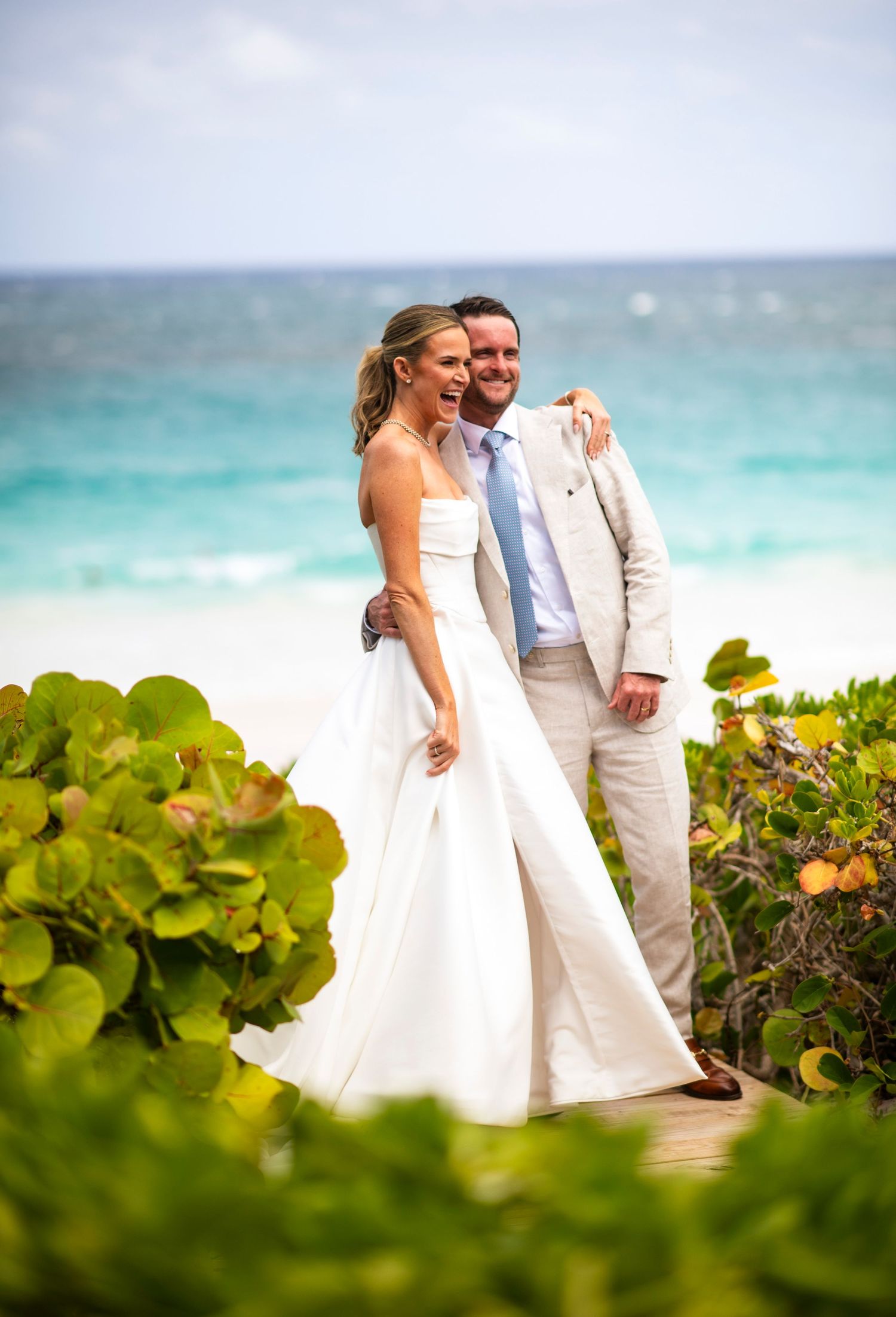 A romantic beach wedding photo shoot with a couple walking along turquoise waters and tropical foliage  on harbour island Bahamas