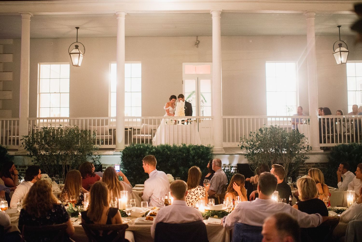 A panoramic view of a formal dining reception setup inside an elegant white ballroom with hanging lanterns.