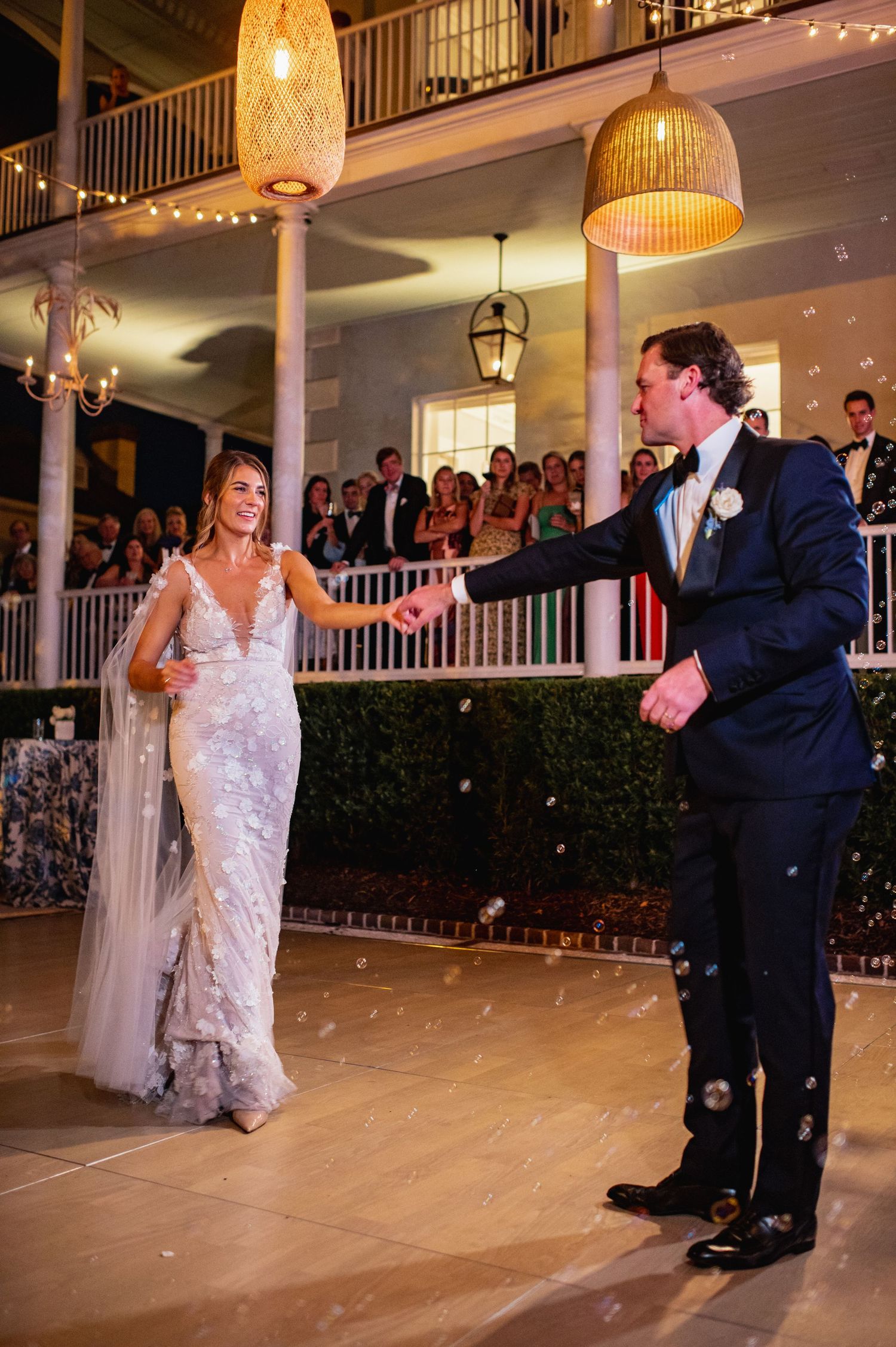 A couple performs their first dance at an elegant wedding reception venue with string lights and balcony onlookers.