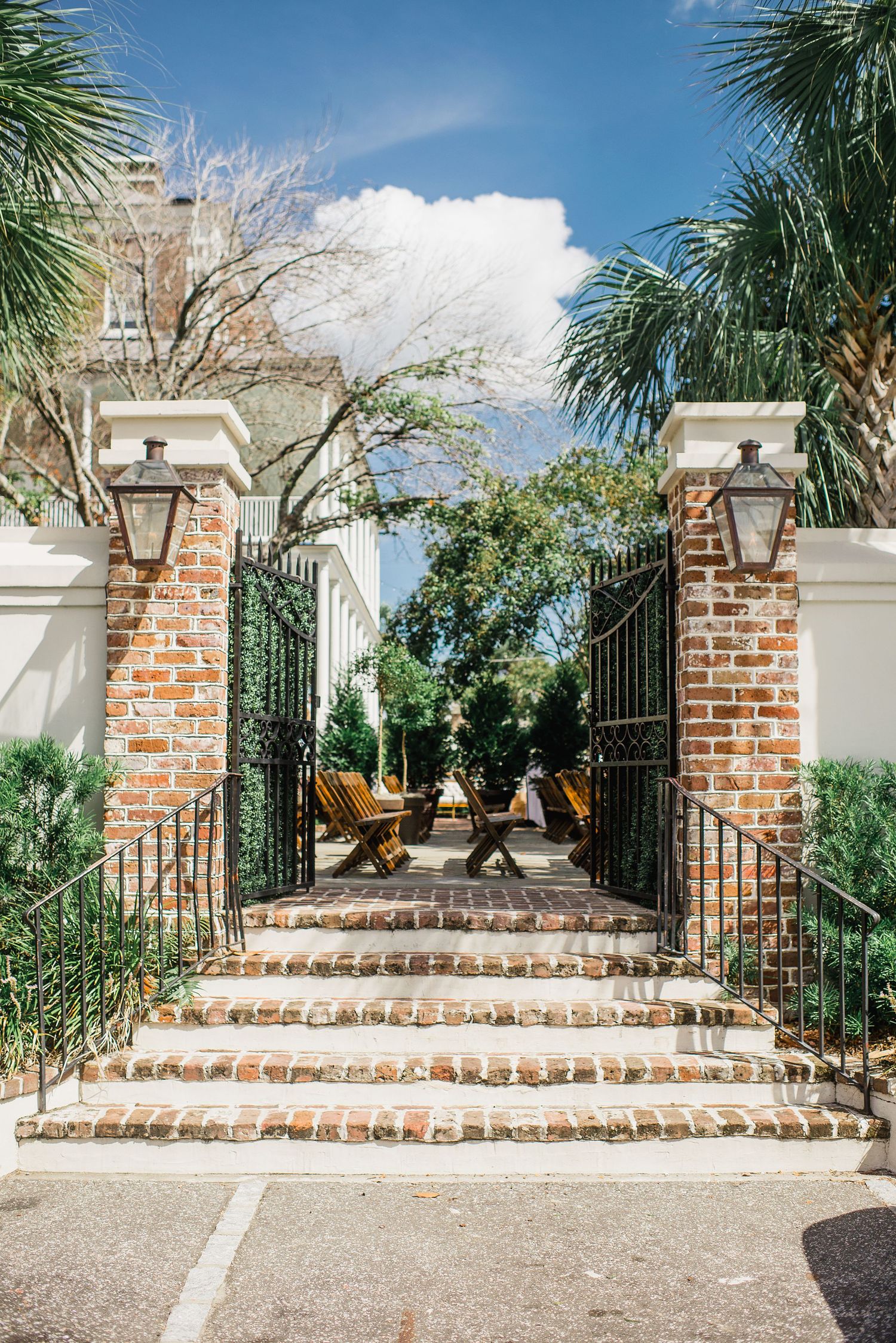 Elegant brick and wrought iron entrance gate with curved steps leading to a tropical garden courtyard.