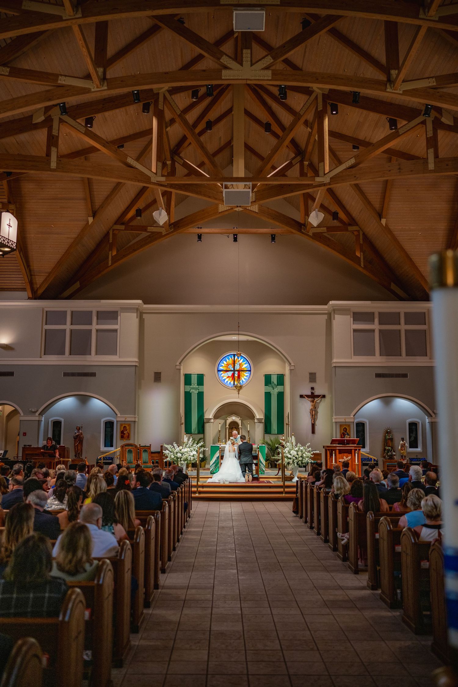 A traditional church wedding ceremony with wooden beam ceiling and guests seated in pews along the center aisle.