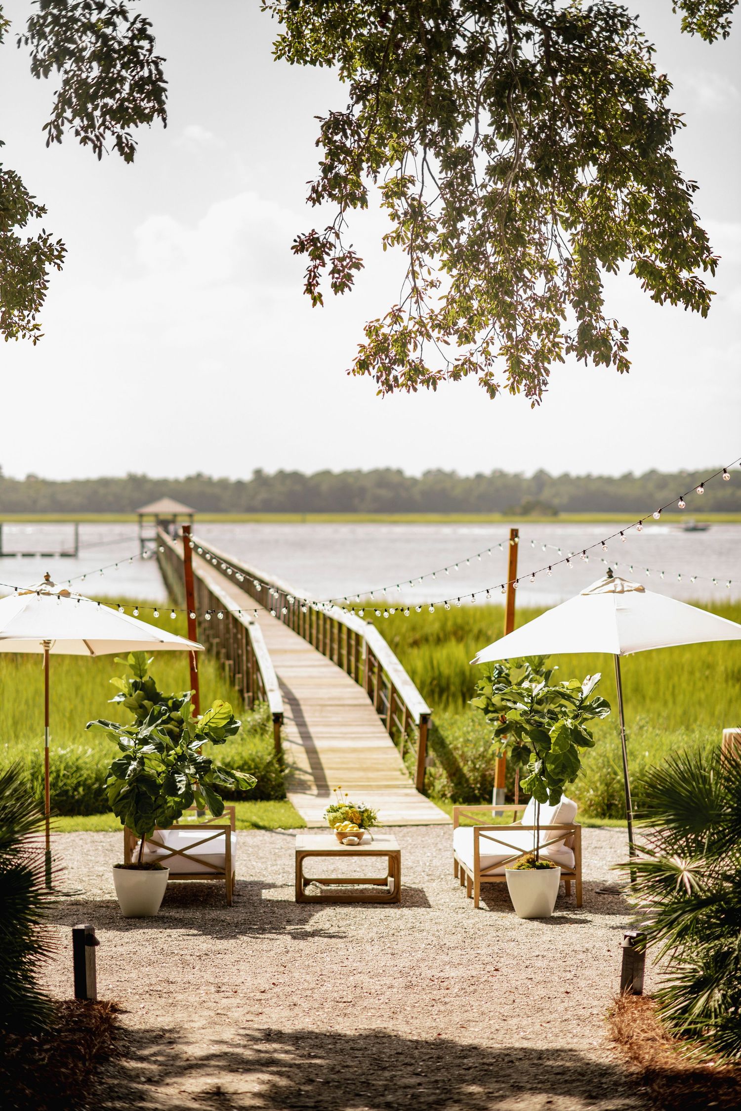 A serene waterfront seating area with wooden boardwalk and deck chairs overlooking a coastal marsh landscape.