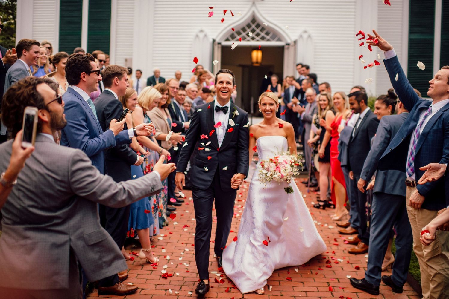 Wedding guests shower the newlyweds with red rose petals during their joyful exit celebration at an indoor venue.