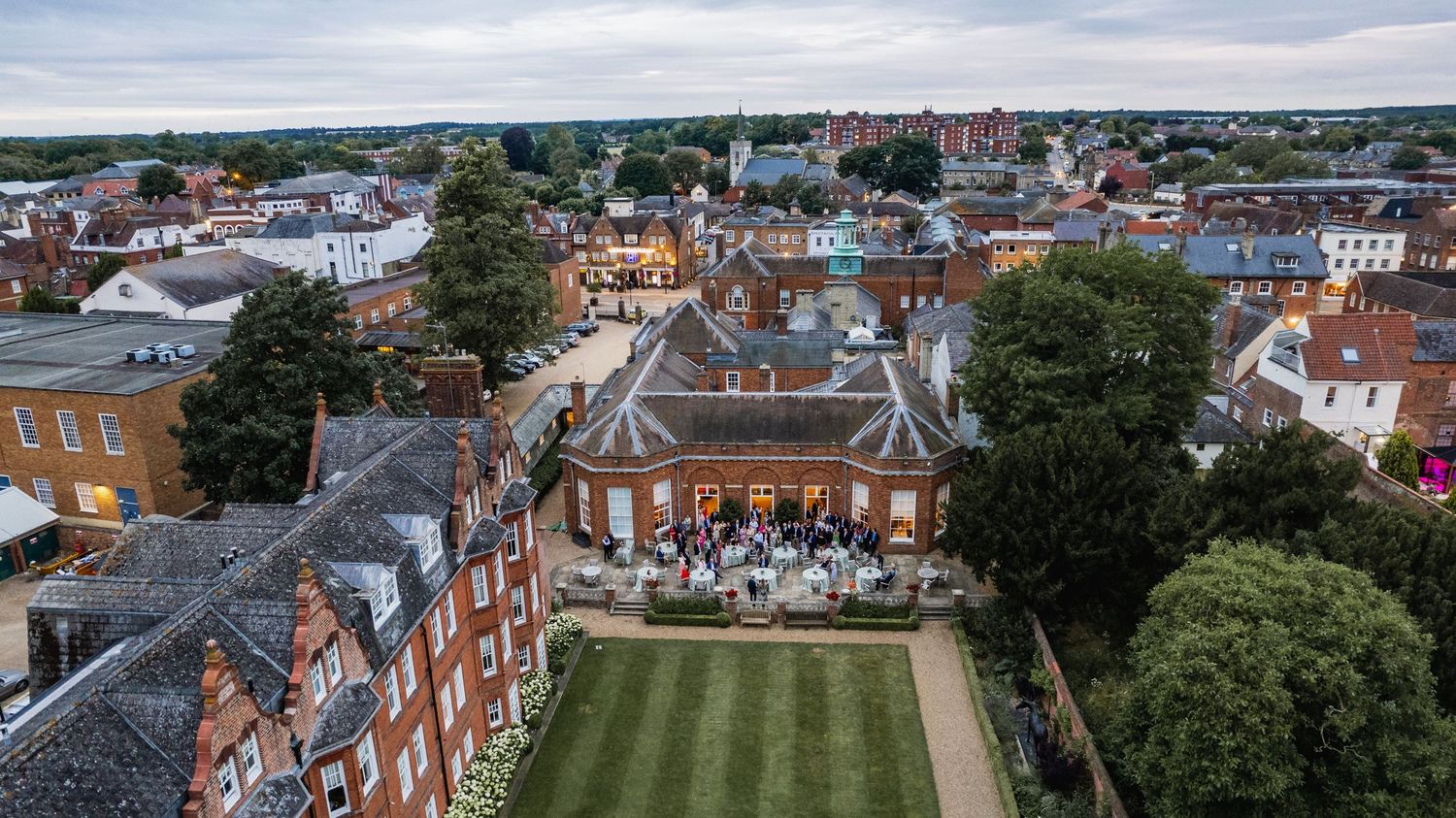 Panoramic aerial view of historic buildings and red-tiled rooftops in an English coastal town with green lawns.