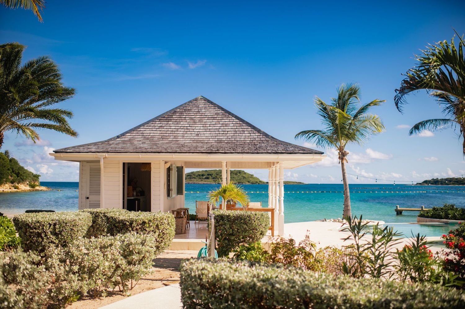 Panoramic view of luxury beachfront villas with palm trees and turquoise ocean waters in a tropical paradise setting.