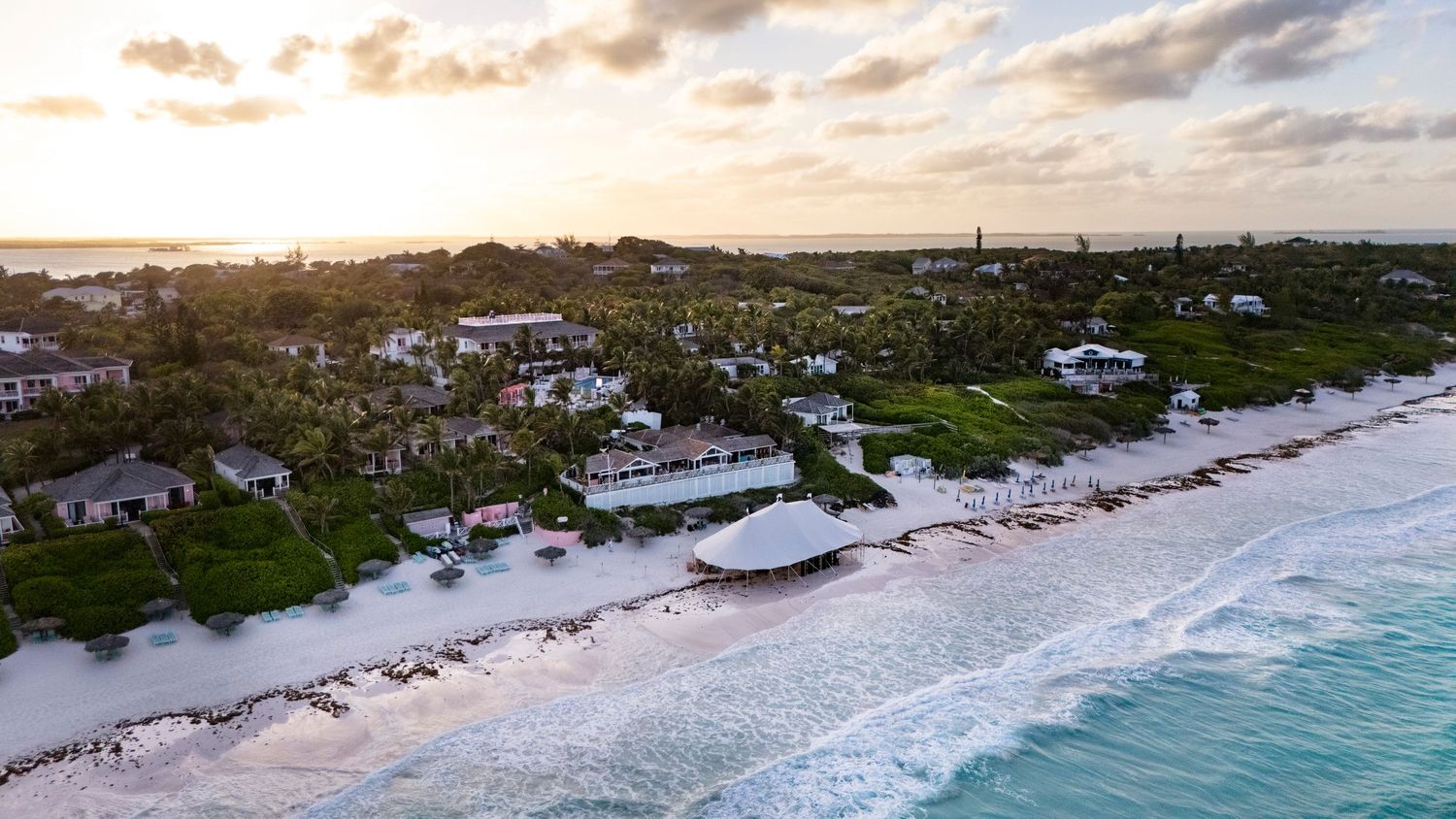 Aerial panoramic view of a beachfront resort with turquoise waters and sandy coastline at sunset.