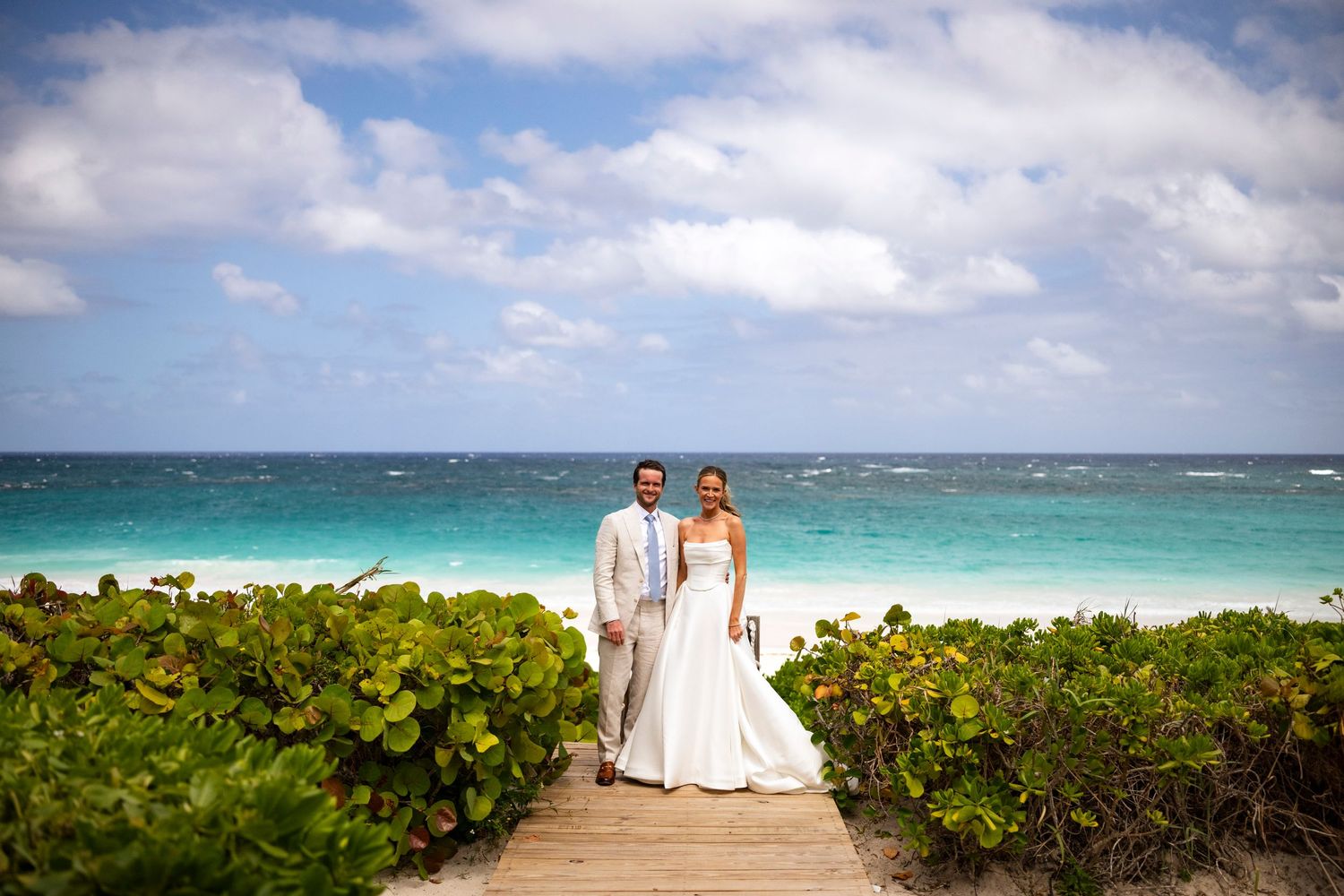 A scenic beachfront wedding ceremony setup with white chairs and tropical foliage along the turquoise ocean shoreline.
