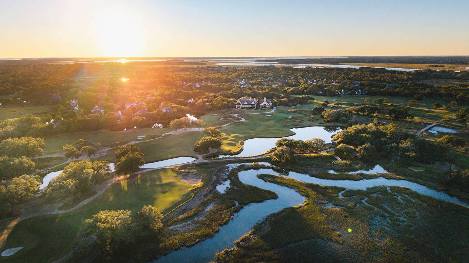 Panoramic sunset view over coastal wetlands with winding waterways and golden light.