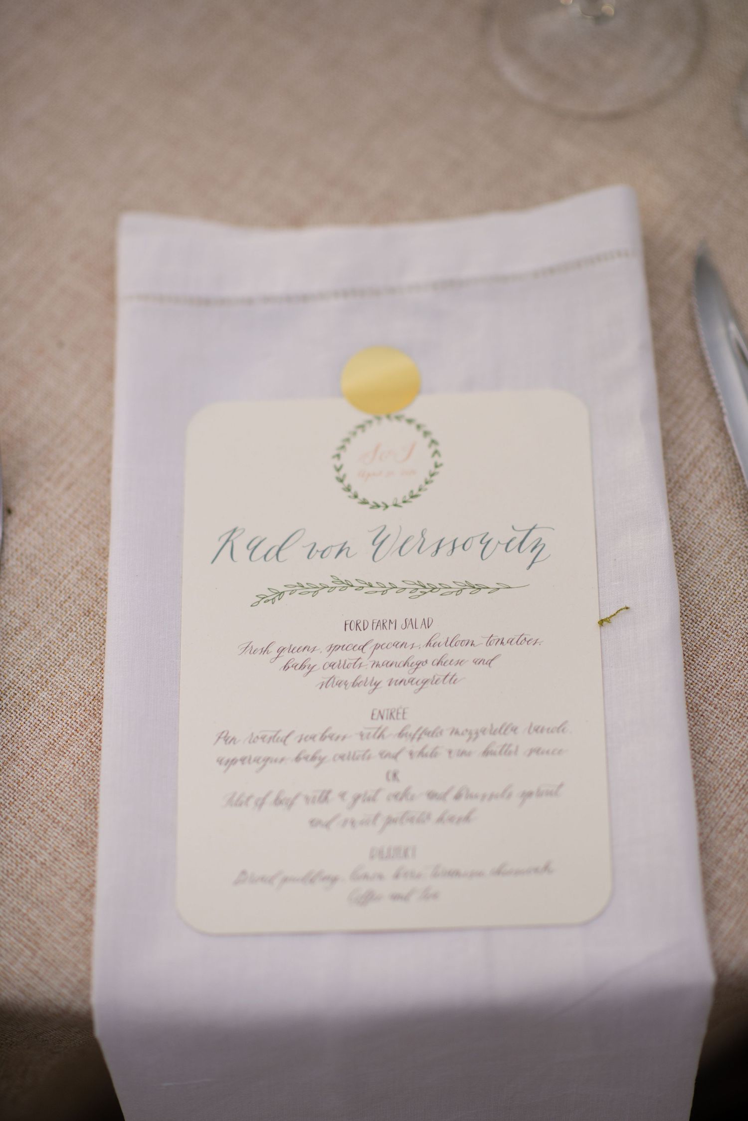 Elegant wedding menu cards with handwritten calligraphy and botanical designs laid out on a beige linen tablecloth.