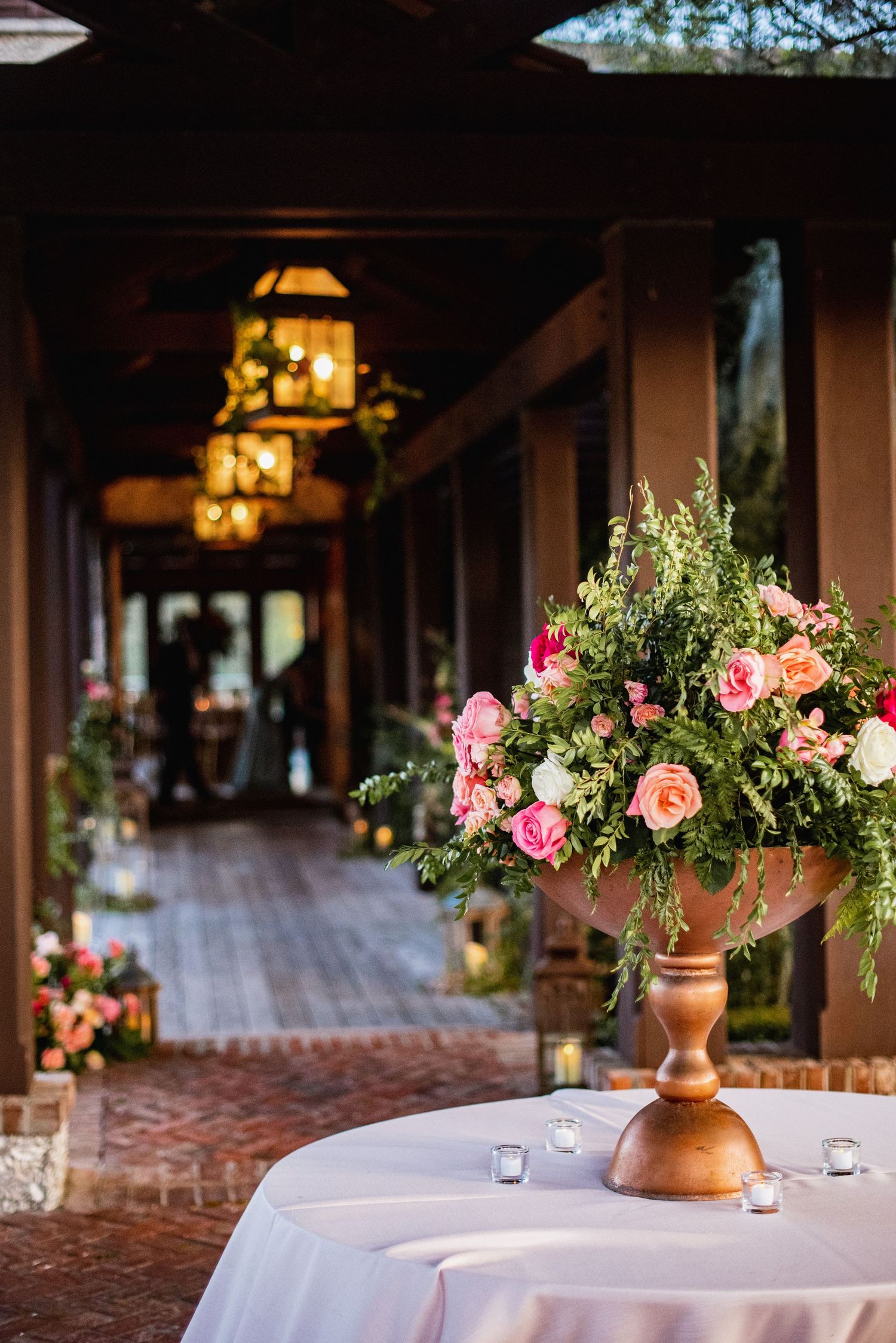 Elegant wedding reception tables decorated with pink floral centerpieces in copper vases and glowing lanterns.