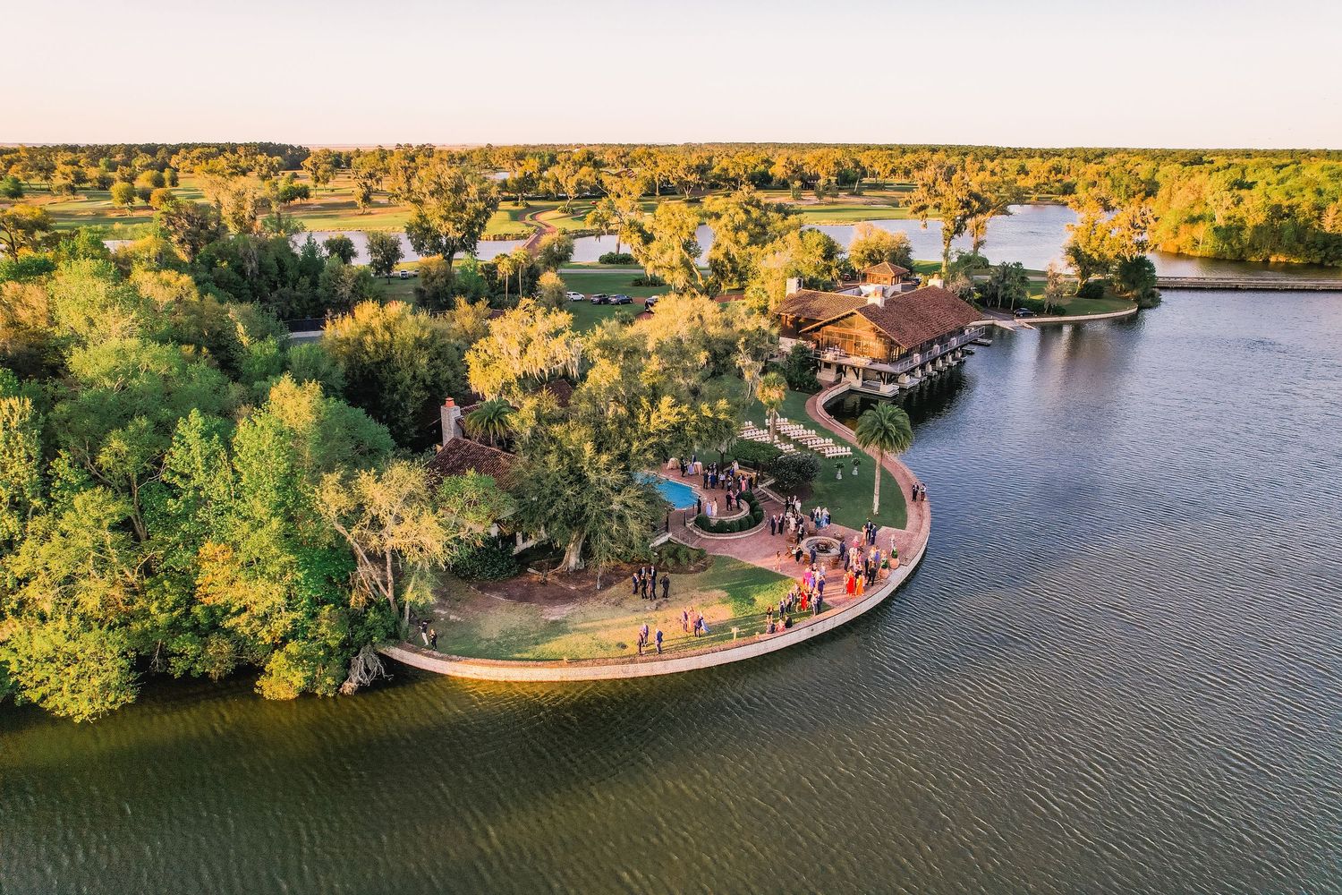 Aerial panoramic view of autumn trees and winding river with boats and docks along residential waterfront property.
