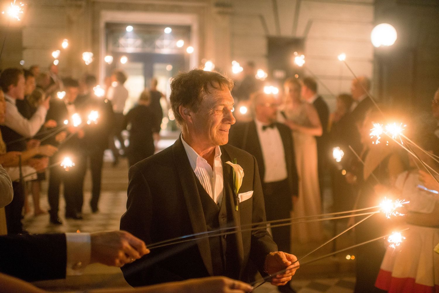 A group of people hold sparklers at an evening celebration creating a magical ambiance with glowing lights.