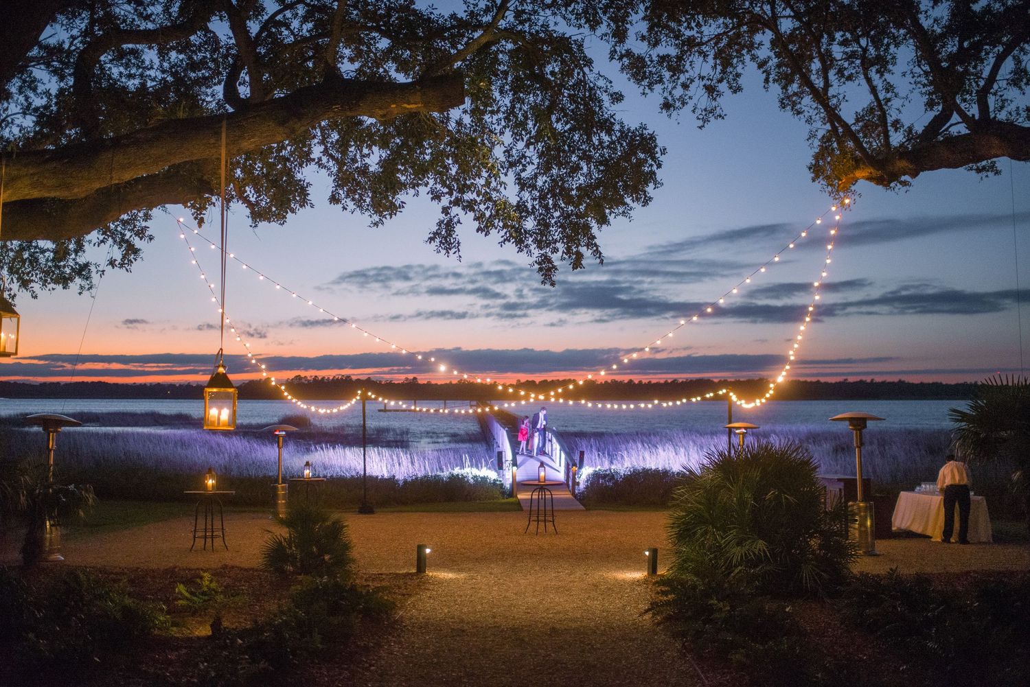 String lights illuminate a waterfront scene at dusk with glowing decorations creating a romantic outdoor atmosphere.