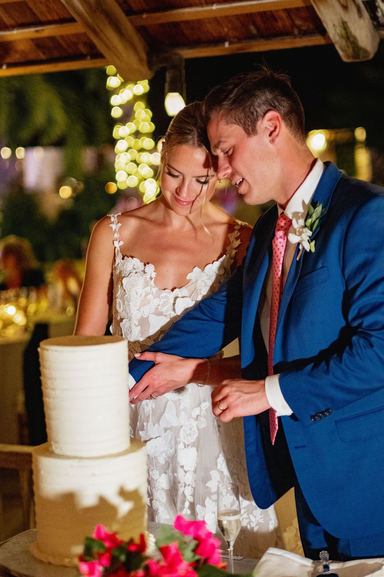 Wedding couple sharing a sweet moment while cutting their white tiered cake.