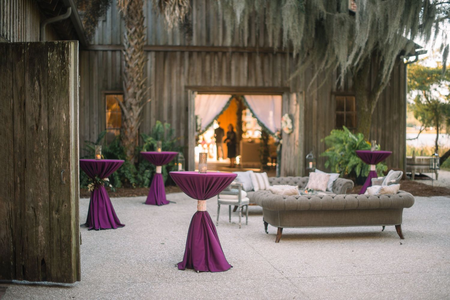 Outdoor event space with purple cocktail tables and rustic wooden walls at sunset creates an elegant ambiance.