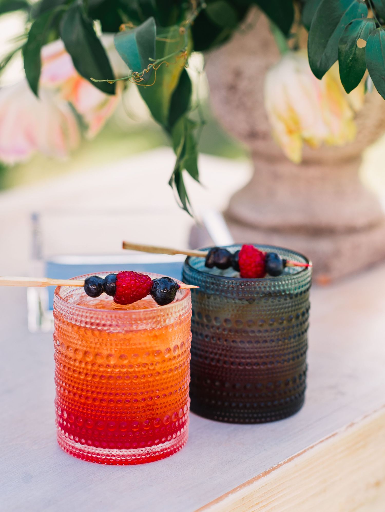 Colorful glass tumblers with ombre effect from orange to red filled with berries and garnishes on a light table setting.